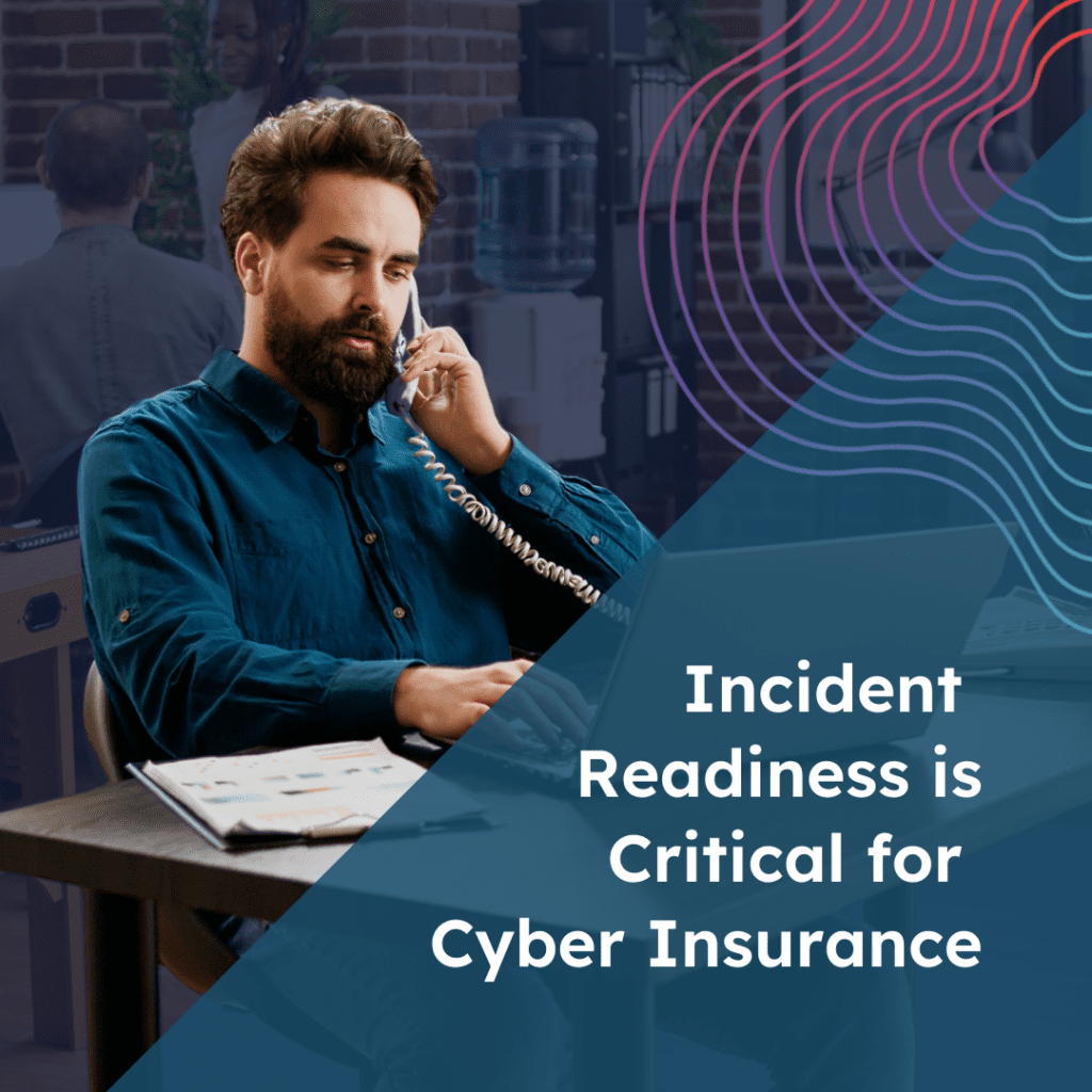 A male ShadowHQ employee in a blue long sleeved shirt sits at a desk holding a phone to his ear, with a quote saying "Incident Readiness is Critical for Cyber Insurance".