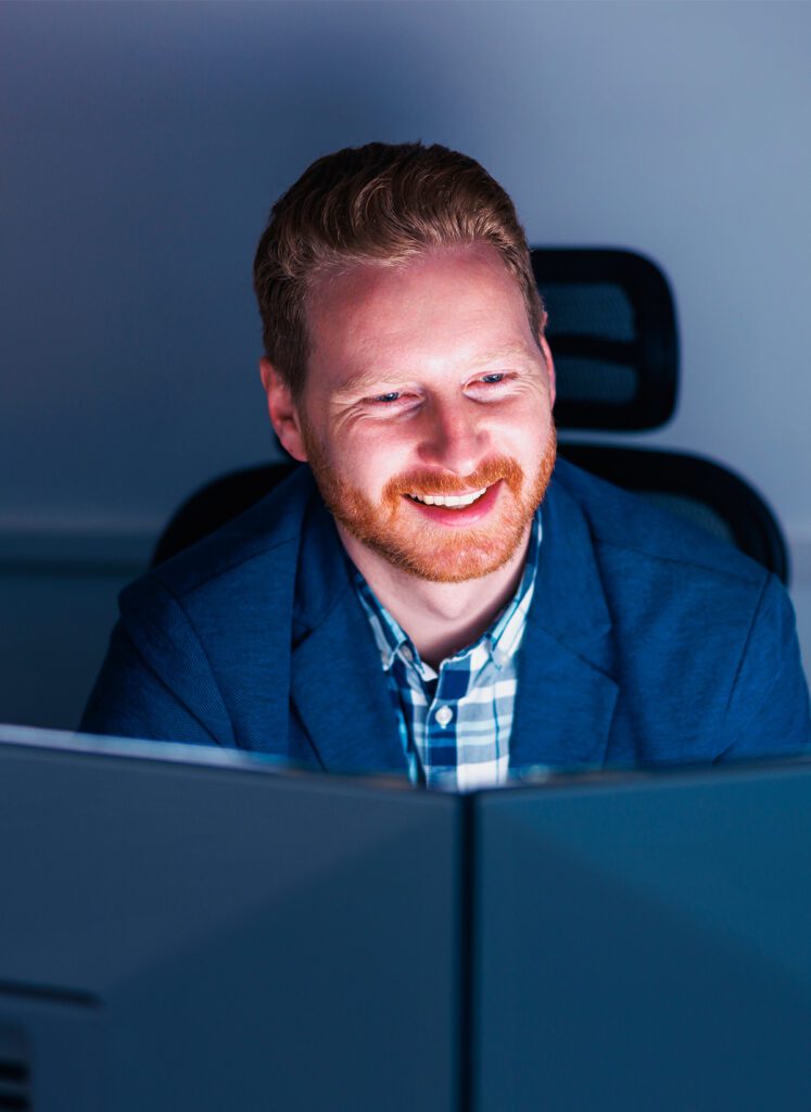 Male ShadowHQ worker smiling while working on double computer monitors